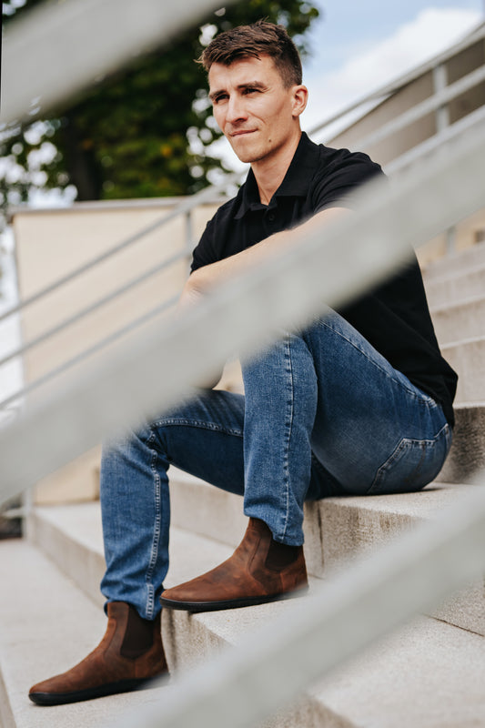Man sitting on steps wearing brown Chalsea style barefoot shoe