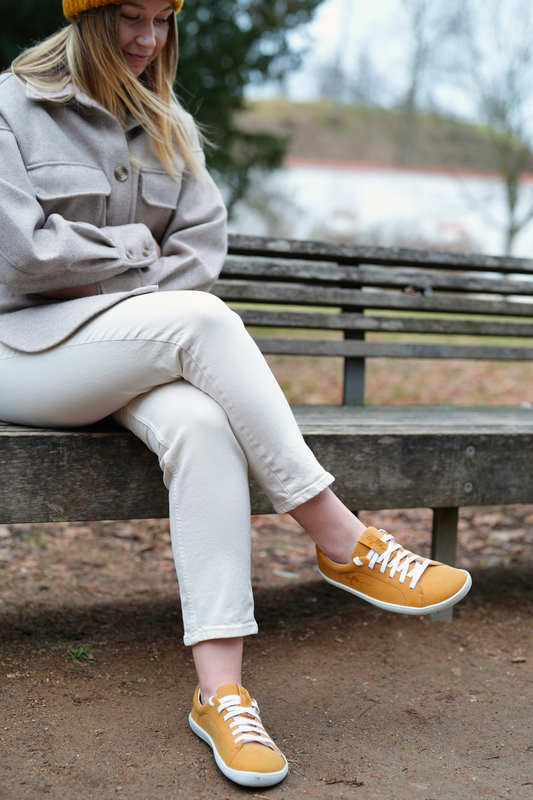 Women sitting on the bench wearing vegan barefoot yellow sneakers.