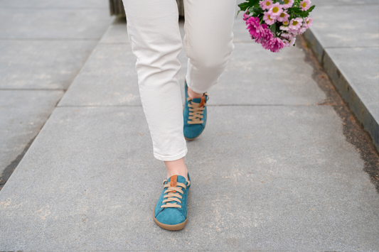 Women walking on sidewalk wearing blue street type of barefoot shoes.